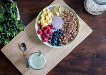 An overhead view of several superfoods in a bowl with a glass of camel milk on the side. These items are on top of wood block.