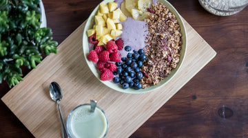 An overhead view of several superfoods in a bowl with a glass of camel milk on the side. These items are on top of wood block.