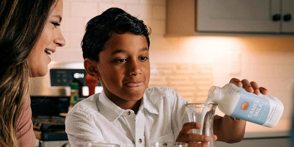 Woman and young boy in a kitchen pouring a bottle labeled 'Calm' into glasses.